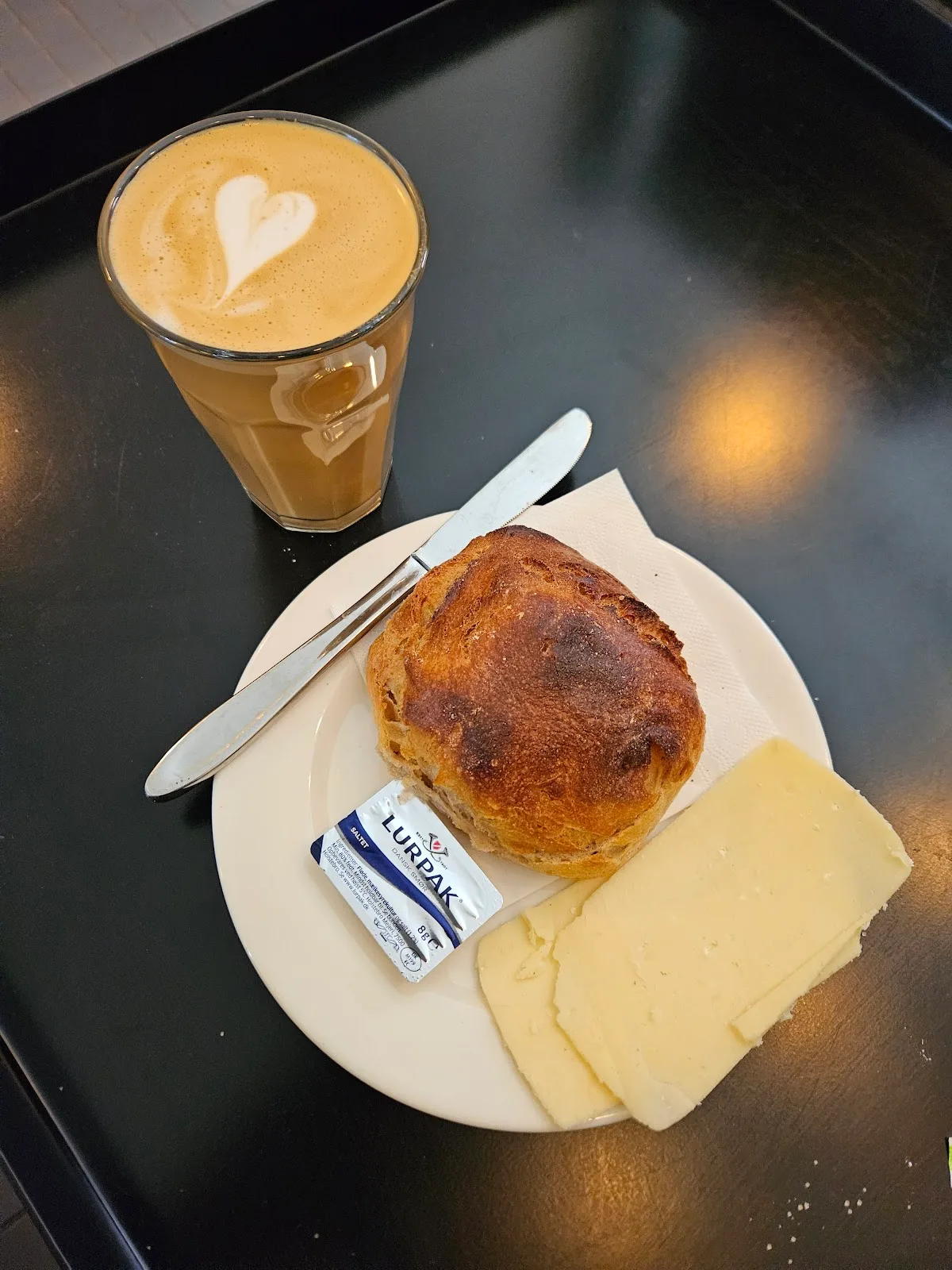 En lun bolle med smør og ost og en latte ved siden af