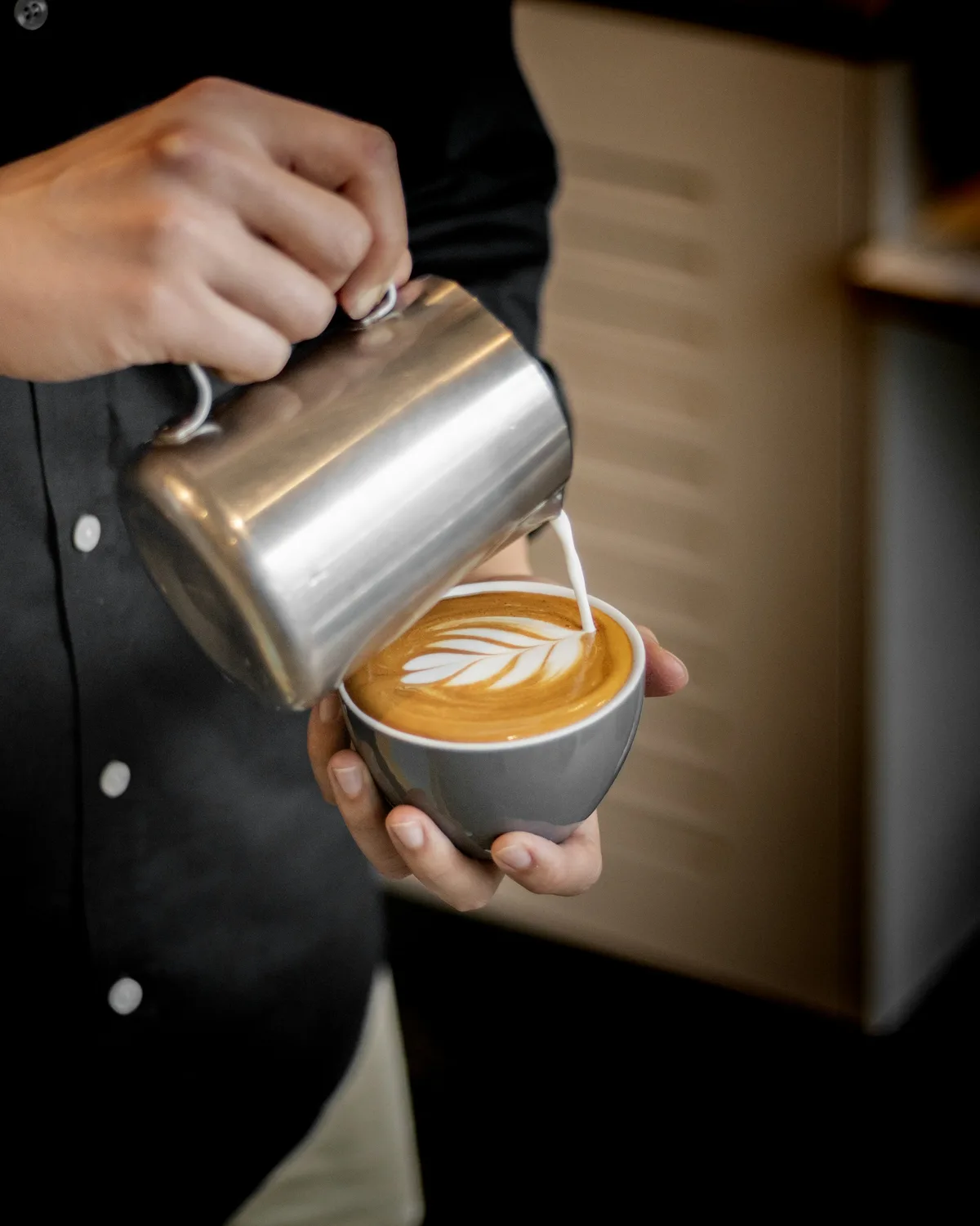 Barista hælder dampet mælk i en latte